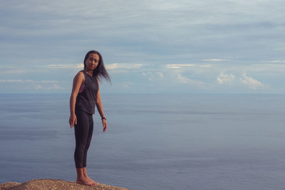 Portrait of young woman standing at sea shore against sky