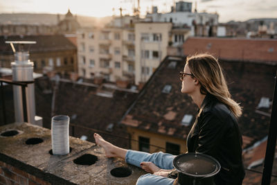 Woman wearing sunglasses while sitting on retaining wall in city