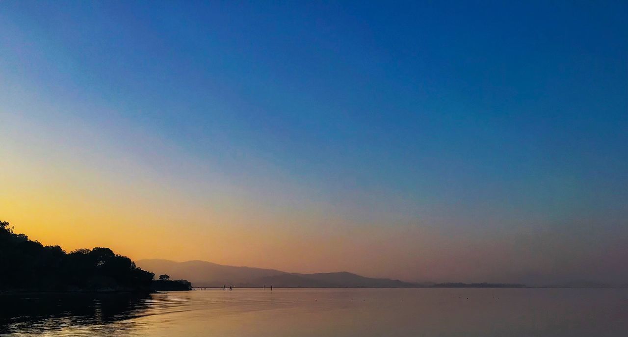 sky, water, scenics - nature, tranquility, beauty in nature, tranquil scene, sunset, waterfront, copy space, clear sky, nature, lake, idyllic, silhouette, no people, blue, orange color, non-urban scene, outdoors