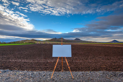 Empty road sign on field against sky