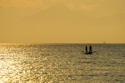 Silhouette people on boat at sea against orange sky