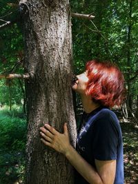 Side view of young woman hugging tree in forest