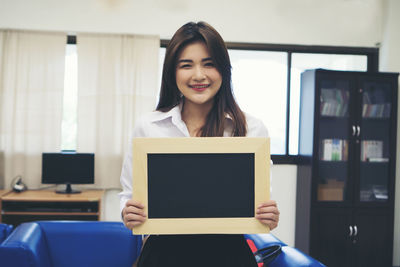 Portrait of smiling businesswoman holding blank slate while standing in office