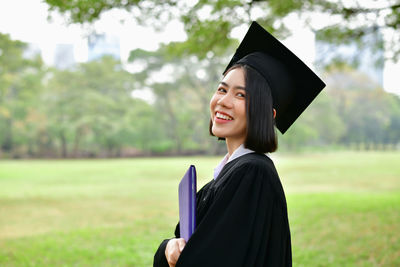 Student wearing graduation gown while standing on field at park