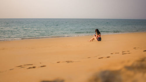 Full length of woman relaxing on beach against sky