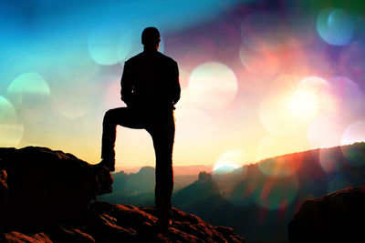 Silhouette man standing on rock against sky during sunset