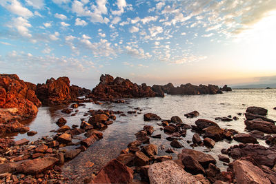 Rocks on beach against sky during sunset