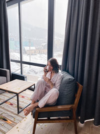 Full length of woman sitting on chair by window