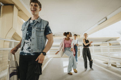 Carefree young male and female friends dancing while walking on footpath of parking garage