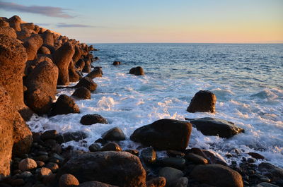 Rocks on beach against sky during sunset