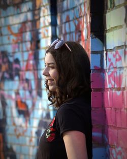 Profile view of woman smiling while standing by graffiti wall