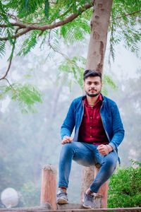 Portrait of young man sitting on tree trunk