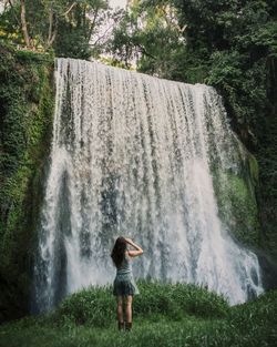Full length of woman looking at waterfall in forest