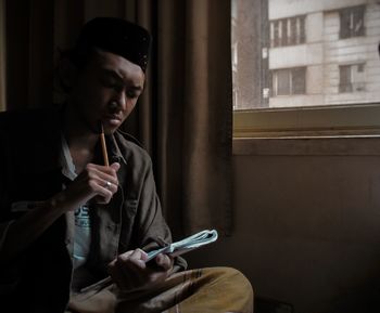 Young man using phone while sitting on window