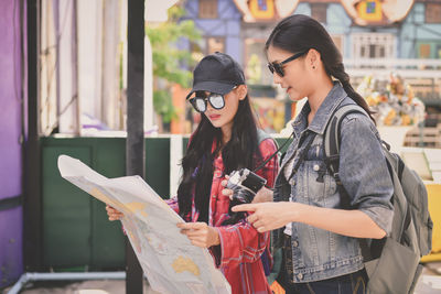 Friends in sunglasses reading map while standing outdoors