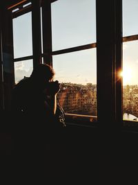 Silhouette man looking through window at sunset