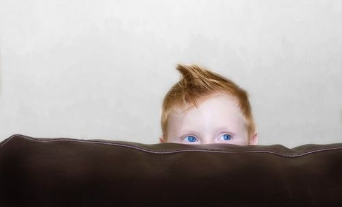 Close-up of boy hiding behind sofa against wall at home