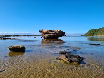 Scenic view of rock formation in sea against clear blue sky