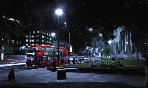 People by bus on illuminated street in city at night