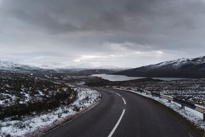 Road leading towards snowcapped mountains against sky