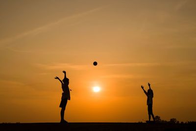 Silhouette friends playing on field during sunset