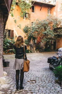 Rear view full length of woman standing on walkway against building in city