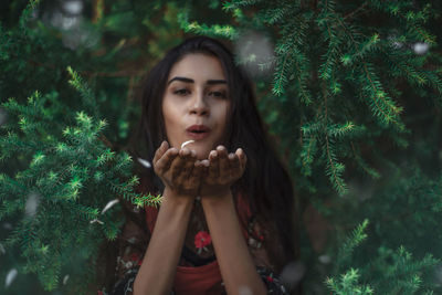 Portrait of beautiful woman holding plants against trees