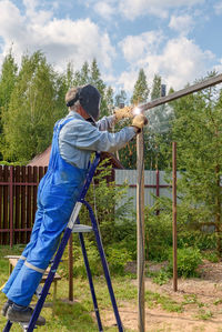 Man welder in a welding mask, construction uniform, protective gloves cooks metal