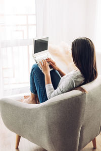 A pretty girl with a laptop is sitting in a soft comfortable chair and working at a laptop