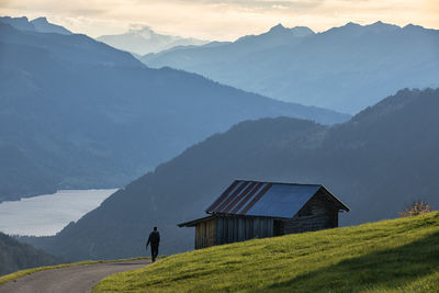 Rear view of man walking by cottage during sunrise