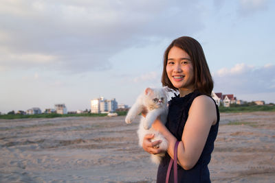 Portrait of smiling young woman with cat standing on sand