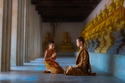 Boy kneeling by monk in buddhist temple