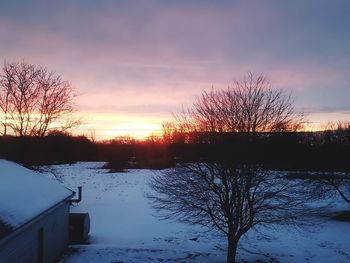 Bare trees by lake against sky during sunset