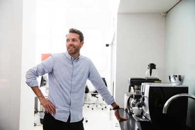 Businessman standing by coffee maker at counter in creative office