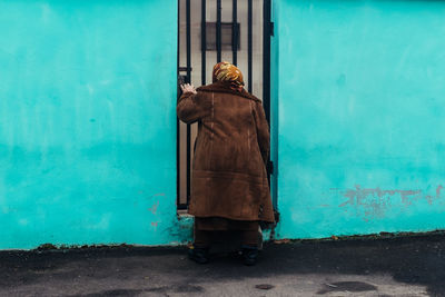 Woman wearing jacket standing at doorway by turquoise wall