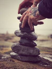 Cropped image of hands with tattoo stacking stones at beach