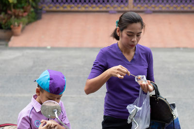 Mother holding food while standing with son on street in city