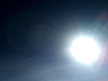 Low angle view of silhouette airplane flying against bright sun