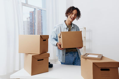 Portrait of young woman holding box while sitting on cardboard boxes