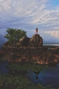 Woman standing on cliff by sea against sky