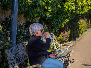 Side view of senior woman drinking water from bottle in park