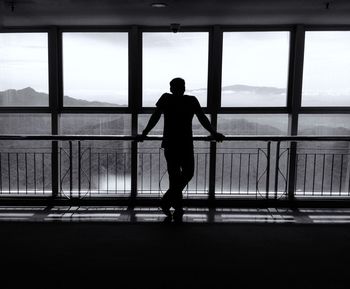 Rear view of silhouette man looking through window