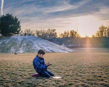 Full length of boy sitting on mobile phone in park