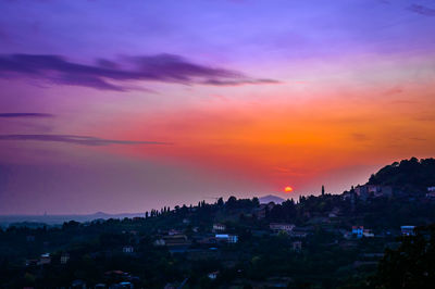 Silhouette houses and trees against sky during sunset