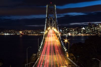 High angle view of light trails illuminated oakland bay bridge and cityscape at night