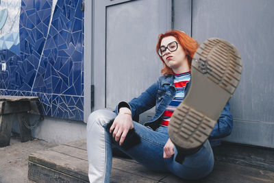 Redhead young woman kicking while sitting against door of building