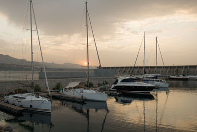 Sailboats moored in harbor at sunset