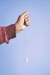 Cropped image of hand dropping coins against purple background