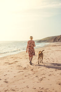 Full length of a girl walking her dog on beach during summer vacation sunset