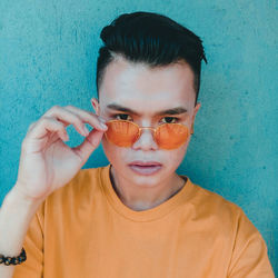 Close-up portrait of young man wearing sunglasses against blue wall